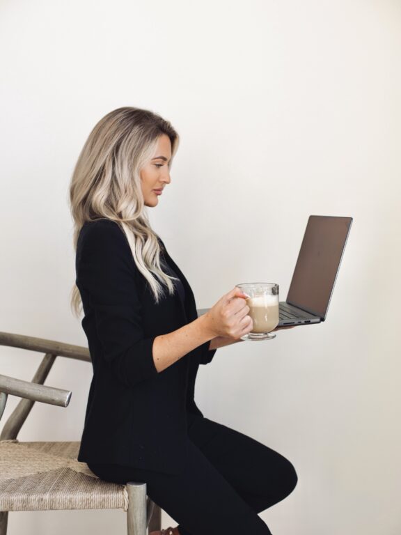 Kayce Sadler, founder of Abode Marketing, working on her laptop with a coffee
