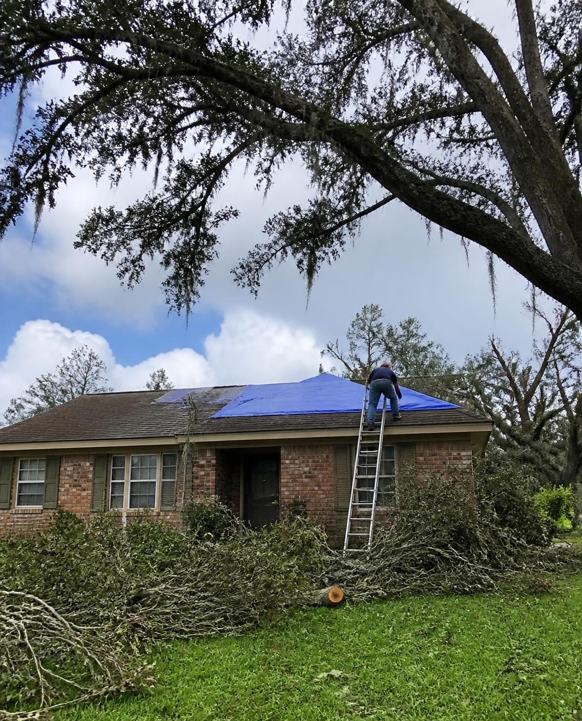 Roofer tarping a storm-damaged roof on a brick home after a Louisiana storm